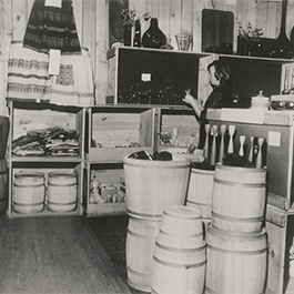A black and white photo of a store showroom with wooden crates and barrels as displays. 
