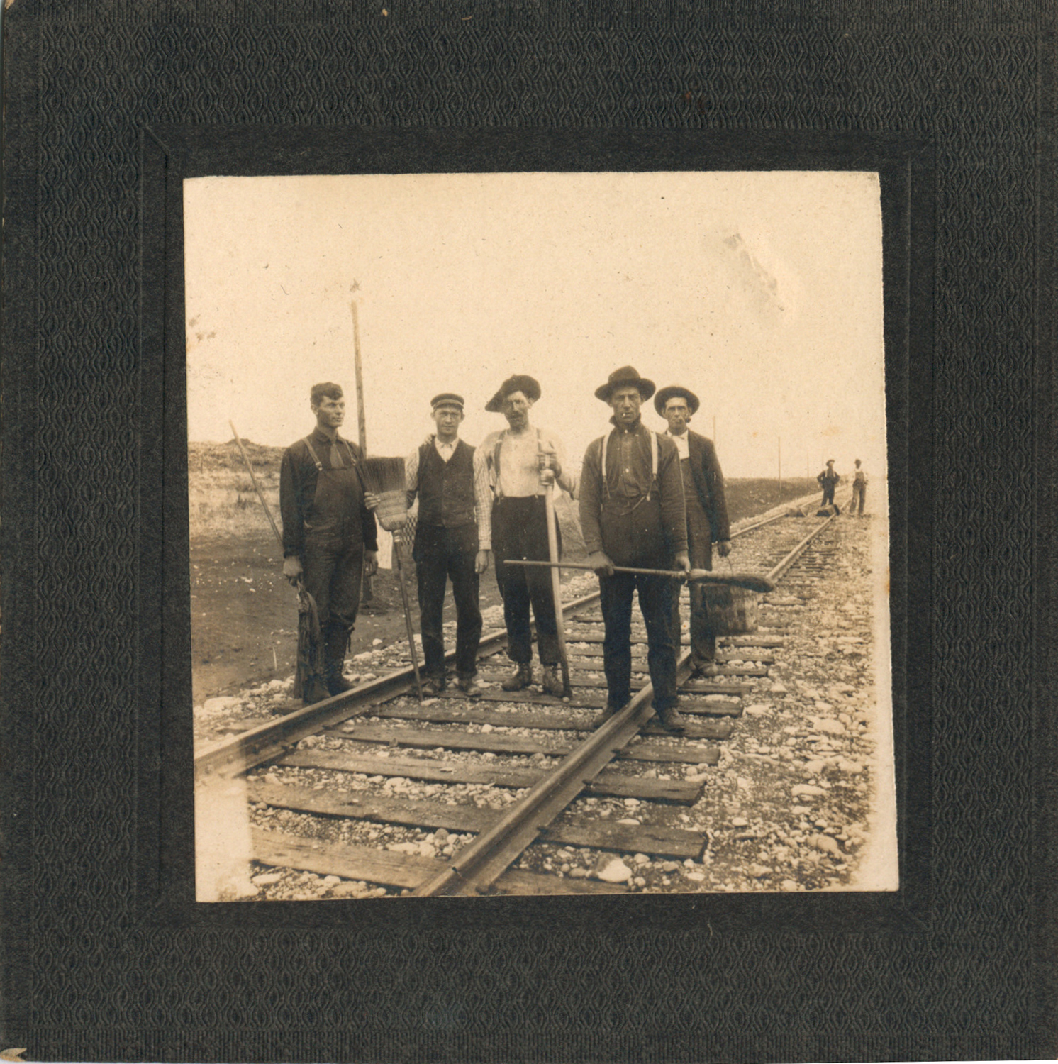 5 men on train tracks, one holding a shovel