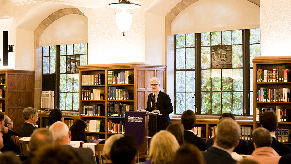 Dohoney at a podium in front of the windows on the first floor of Deering Library