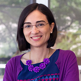 A woman with dark chin length hair and rimless glasses smiles at the camera